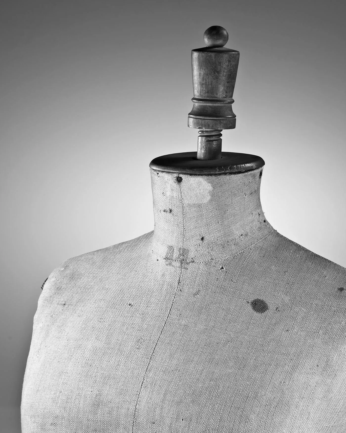 The neck and shoulder of an antique linen dress form under even studio light.
