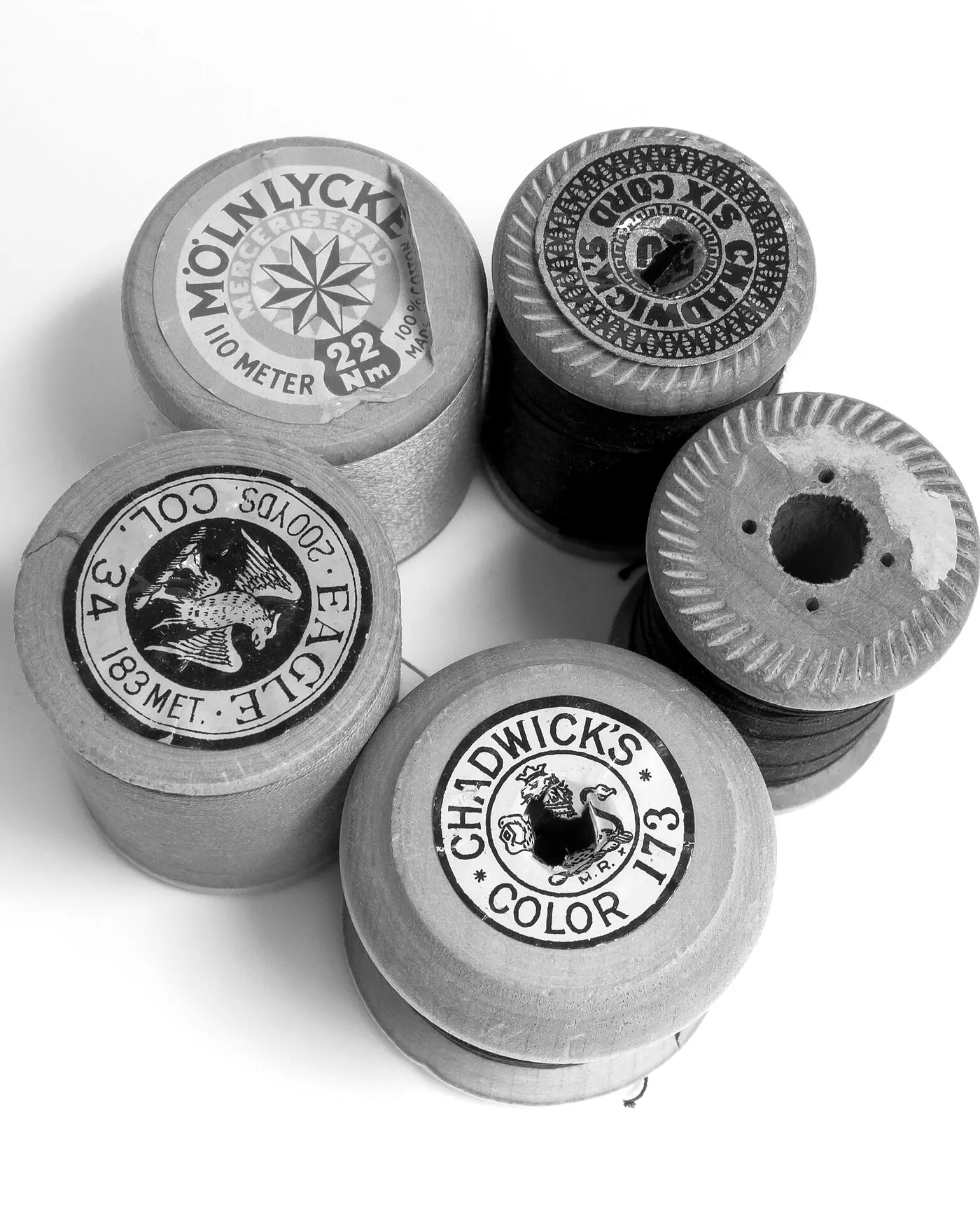 Six wooden spools of thread gathered on a white ground, their labels facing up.