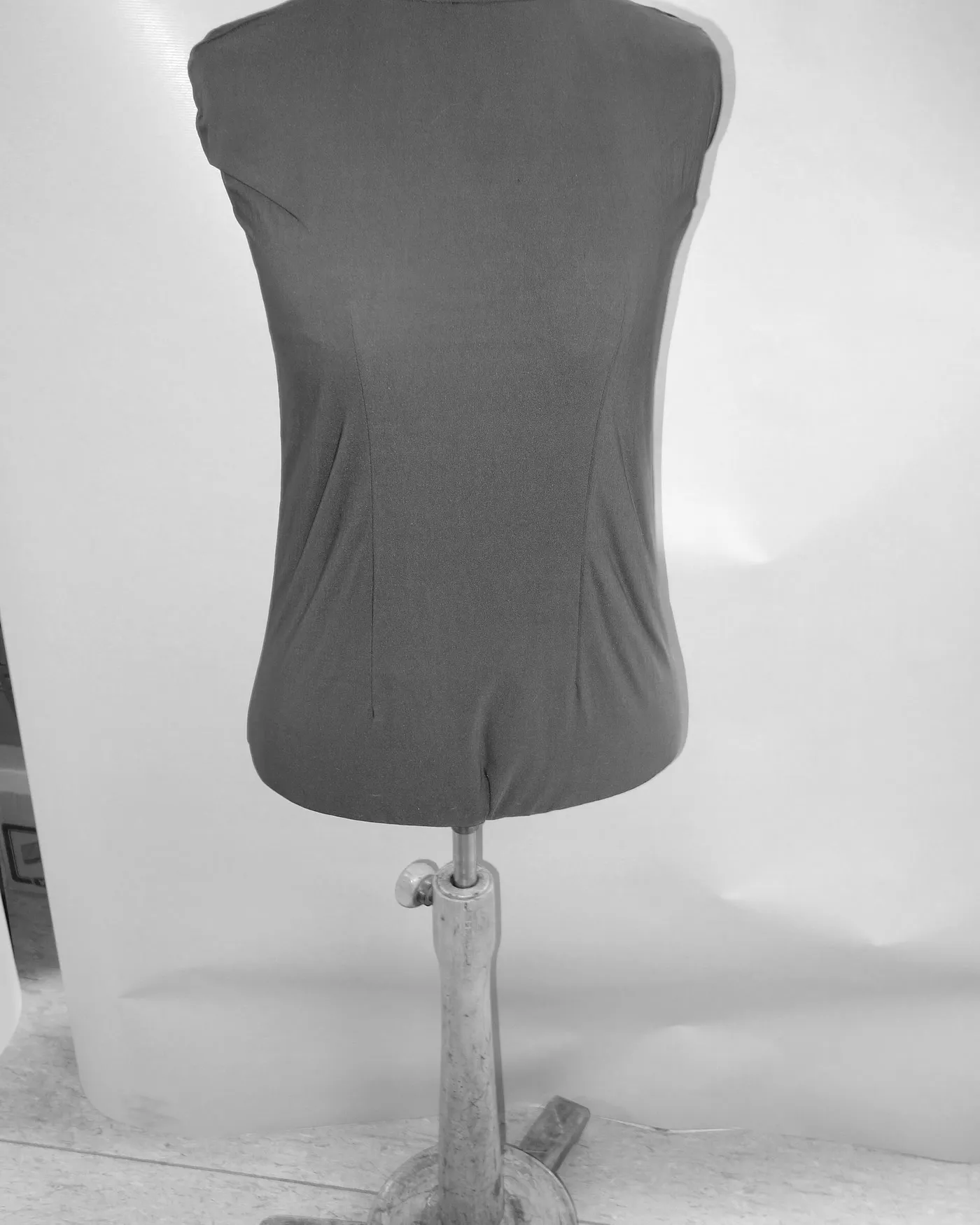 A dressmaker's form covered in plain linen, standing against a lit white backdrop.