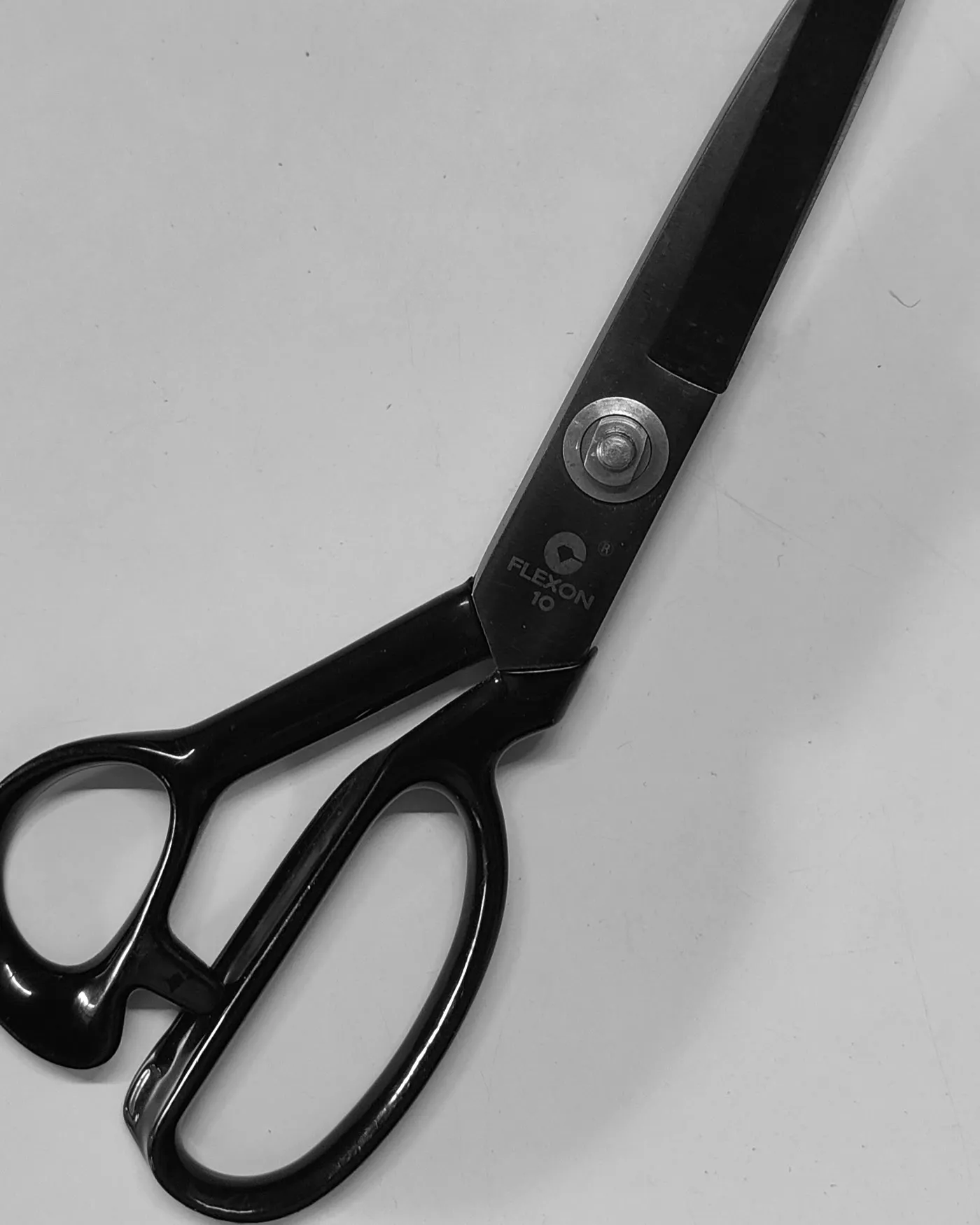 A pair of heavy tailor's shears resting open on a pale surface.